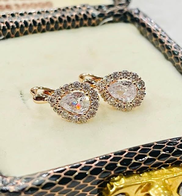 Pair of dainty 14k rose gold stud earrings featuring pear-shaped white stones encircled by a sparkling halo.