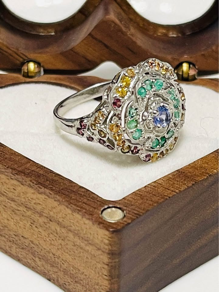 Side angle view of a rose-shaped sterling silver ring featuring a central tanzanite stone with peridot and emerald.