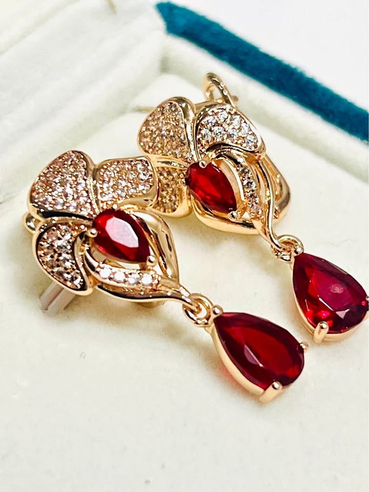 Top-down view of 14k 585RG stamped rose gold dangle earrings with red fancy gemstones and clear accents.
