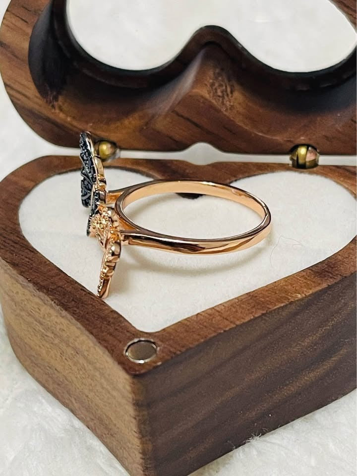Side view of a rose gold butterfly ring with intricate blue and clear pave detailing, in a jewelry box.