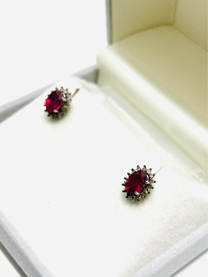  Angled view of classic ruby and diamond stud earrings in a jewelry box, highlighting their precious stones.