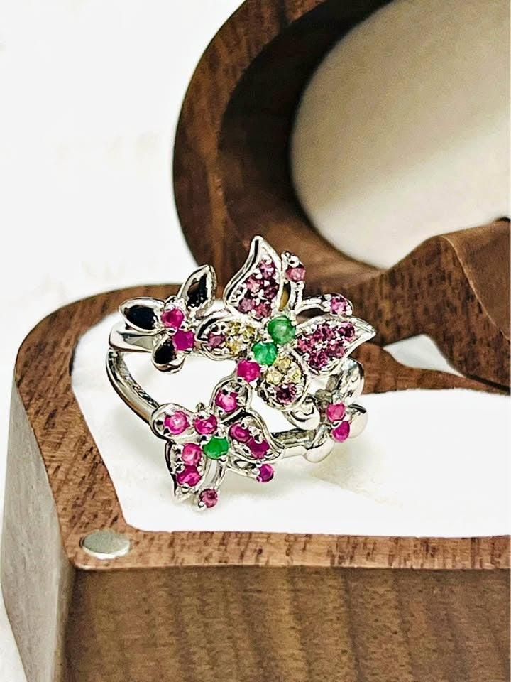 Angled close-up of a silver butterfly ring featuring vibrant natural rubies and emeralds.