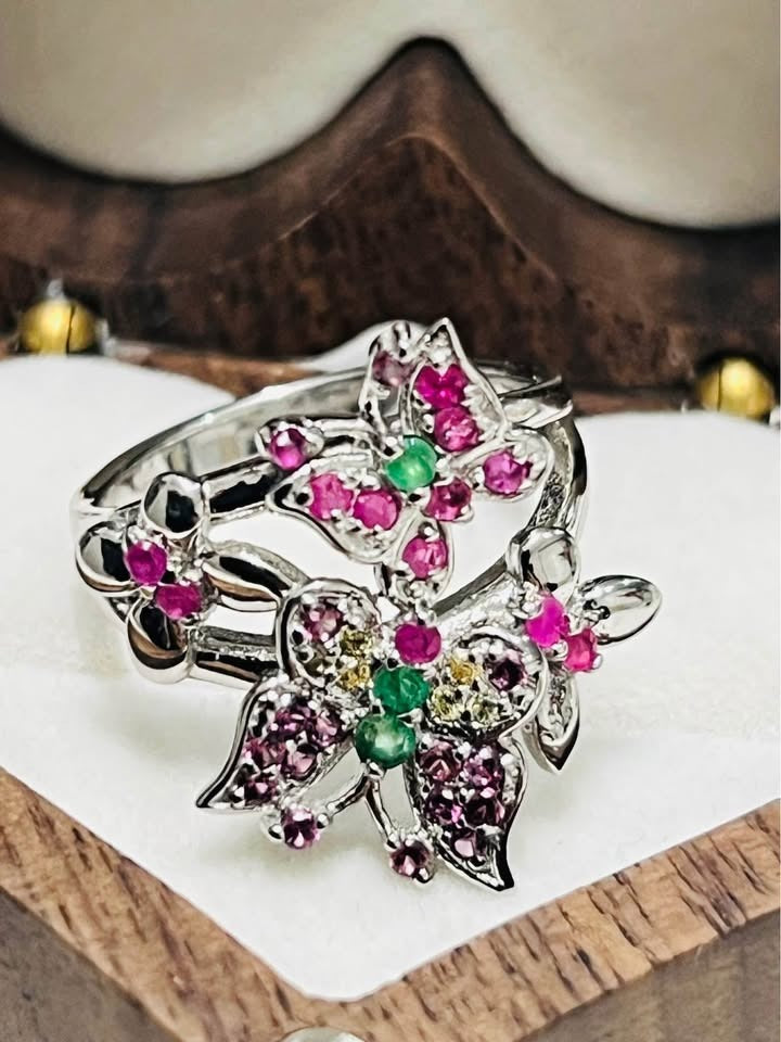 Close-up of a beautiful silver butterfly ring embellished with natural rubies and emerald gemstones.
