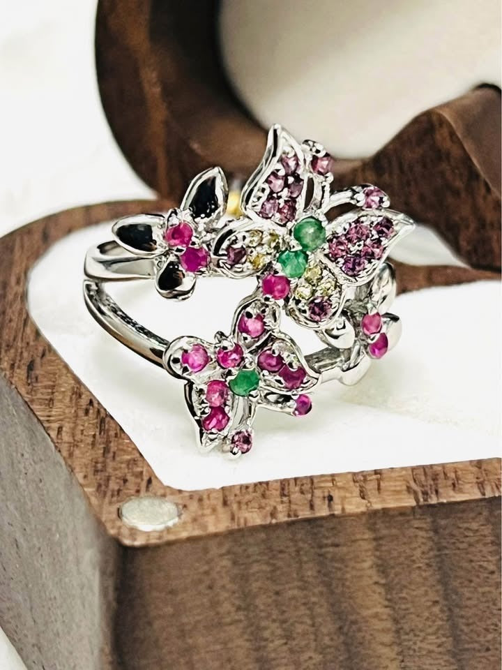 Detailed shot of a natural ruby and emerald butterfly ring in silver, highlighting stone placement.