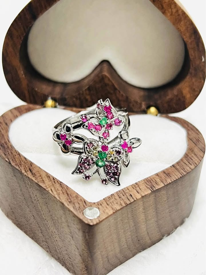 Front view of a sterling silver butterfly ring adorned with natural ruby and emeralds, in a gift box.