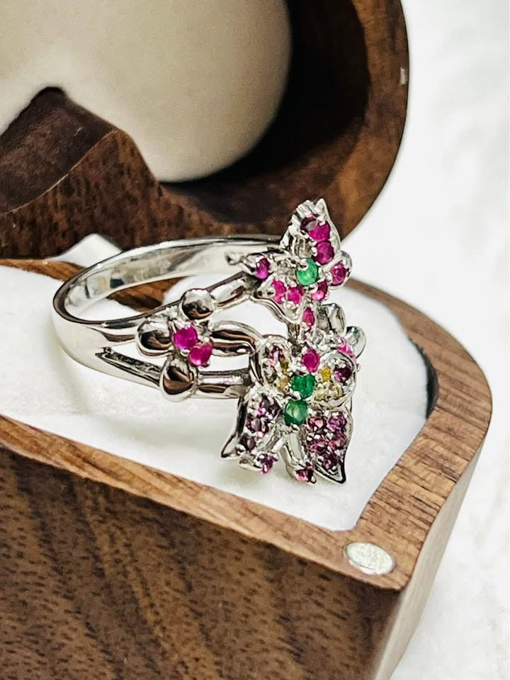 Side view of a silver butterfly ring with natural ruby and emerald gemstones, in a heart-shaped box.