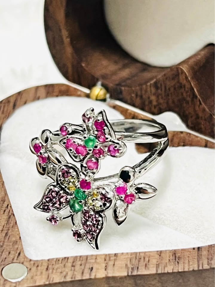Top-angled view of a colorful butterfly ring with natural rubies and emeralds, in a jewelry box.