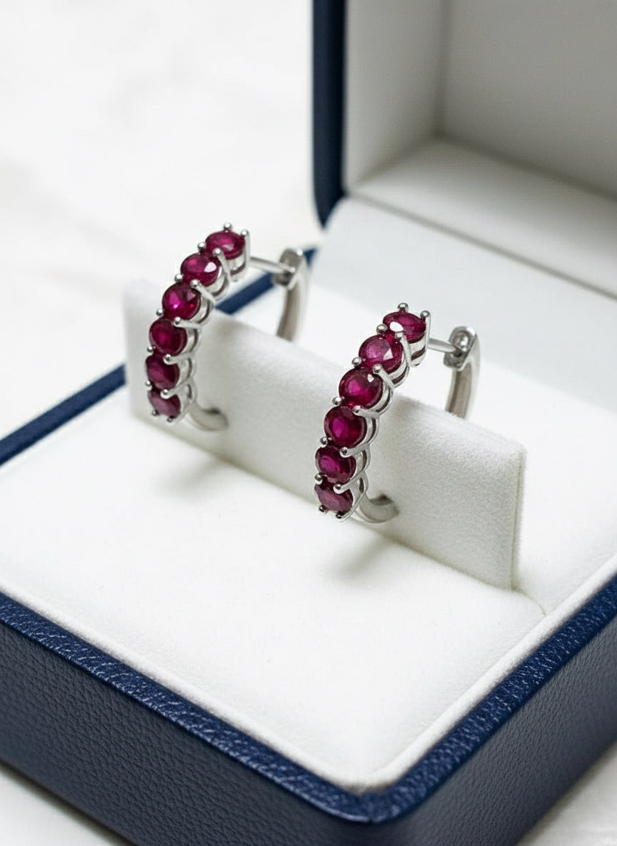 Angled view of natural ruby sterling silver huggie hoop earrings on a white display stand within a box.