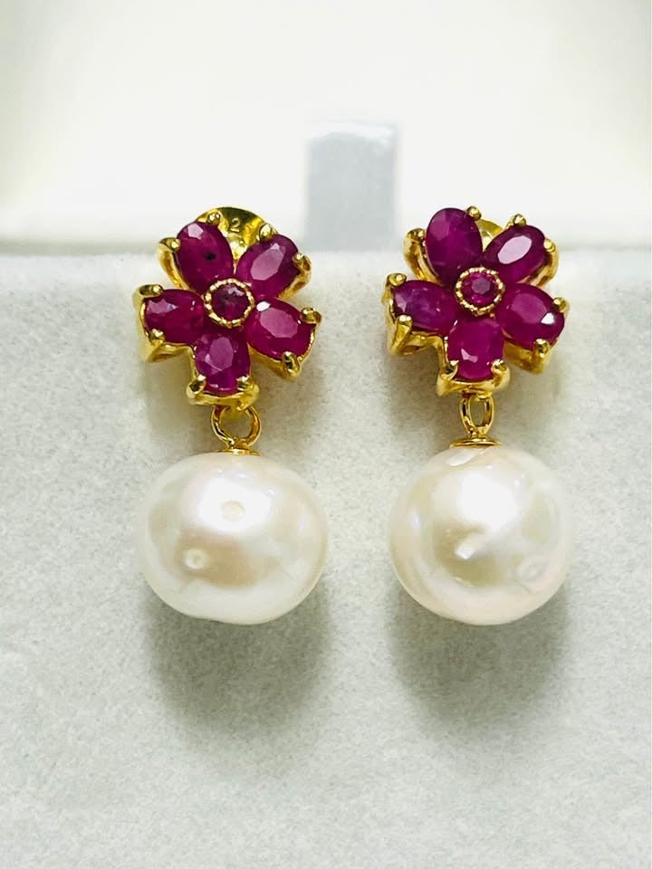 Close-up of natural pink ruby and genuine South Sea pearl dangle earrings, showcasing vibrant color and luster.