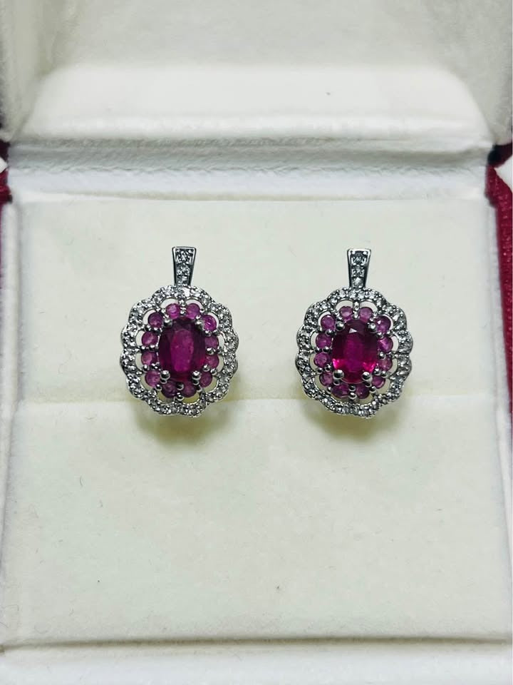 Rhodium-plated sterling silver ruby halo earrings, each featuring an oval ruby and sparkling gem halo, in a jewelry box.