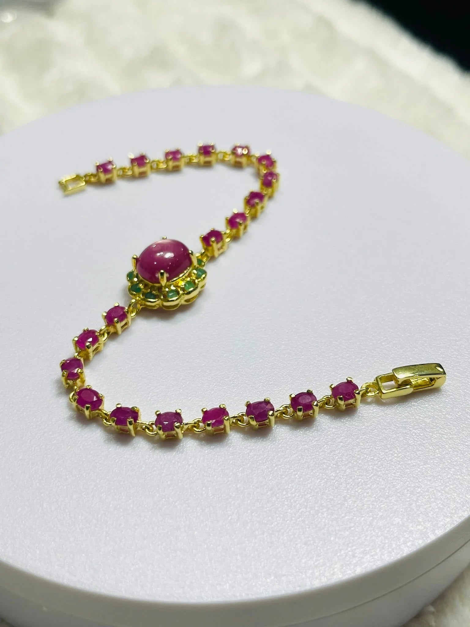 Curved gold bracelet with vibrant oval rubies, a prominent ruby cabochon, and green emerald details.