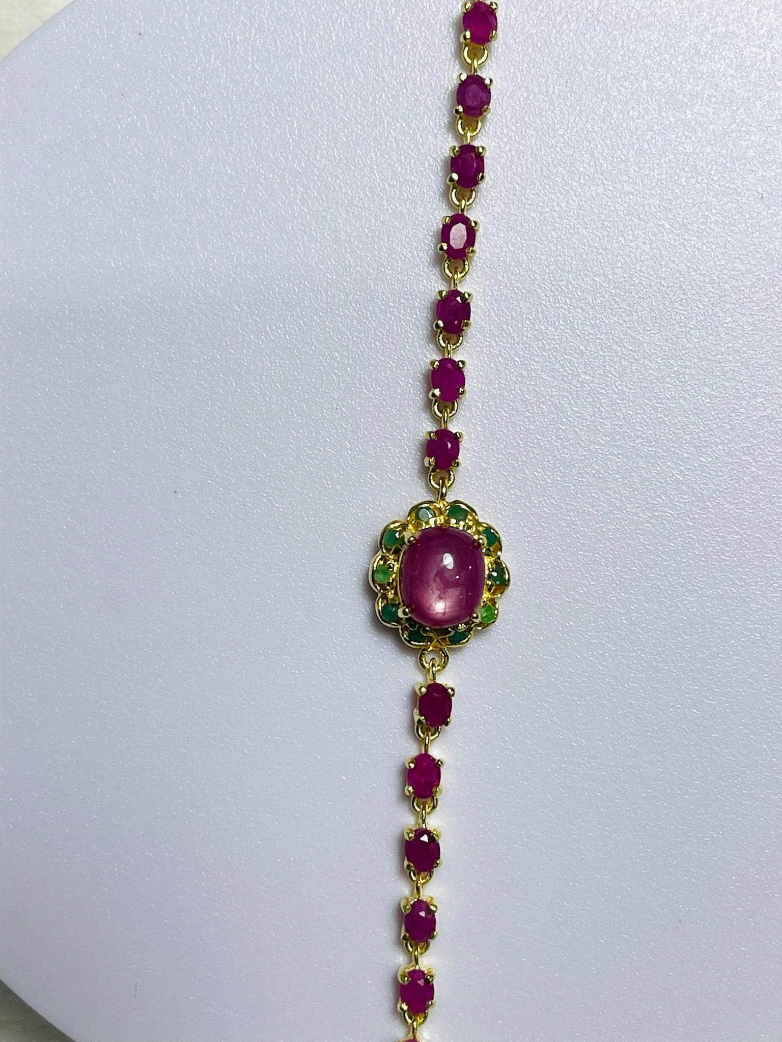 Sophisticated gold bracelet vibrant oval rubies and captivating central ruby/emerald centerpiece, displayed vertically.