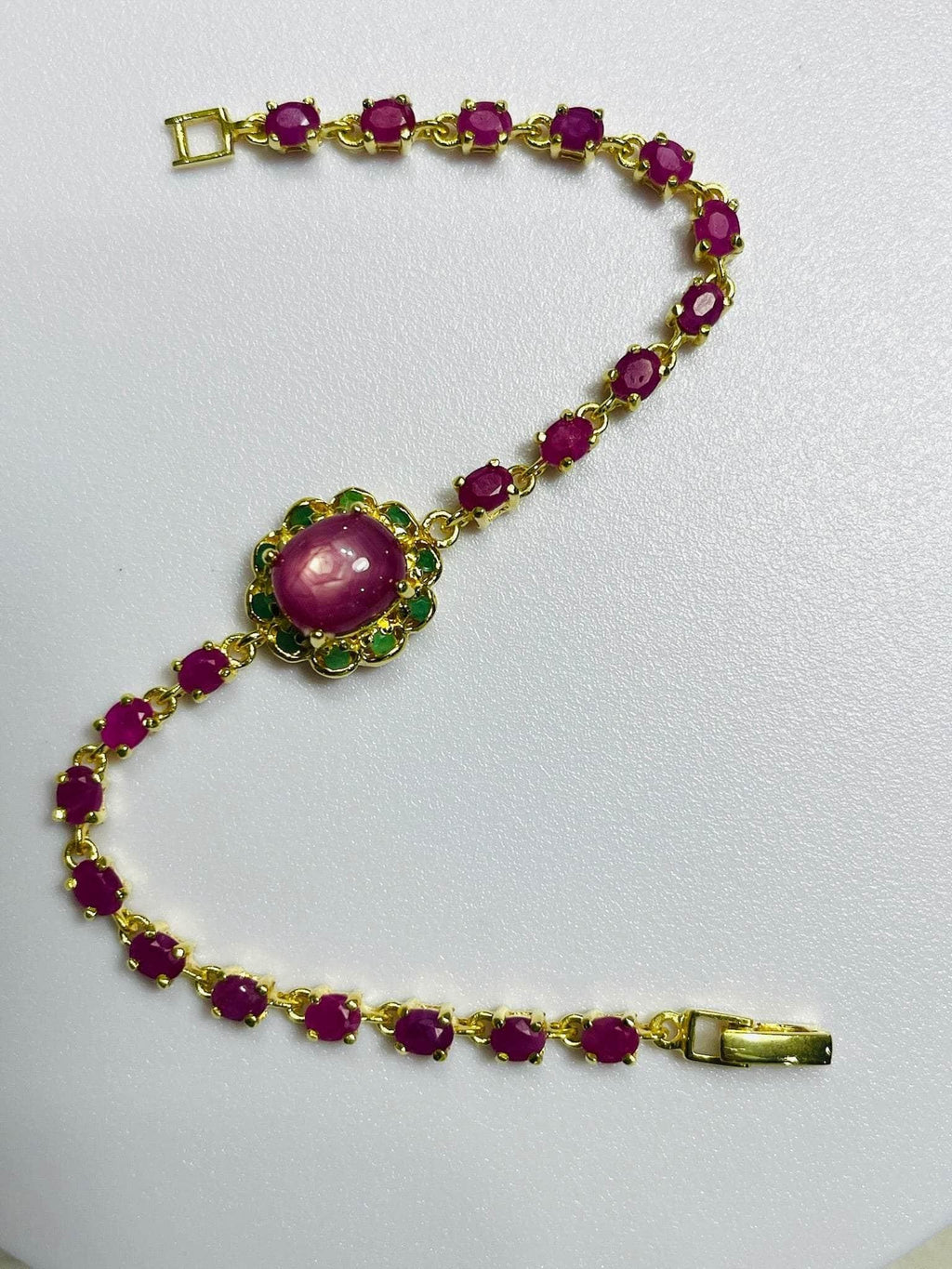 Elegant gold bracelet with oval rubies and a central ruby-emerald cluster, flat on white. 