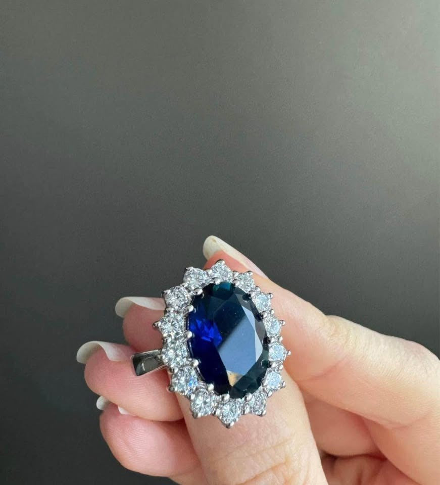 Stunning sapphire Diana ring held by a hand, showing the iconic halo and deep blue gemstone.