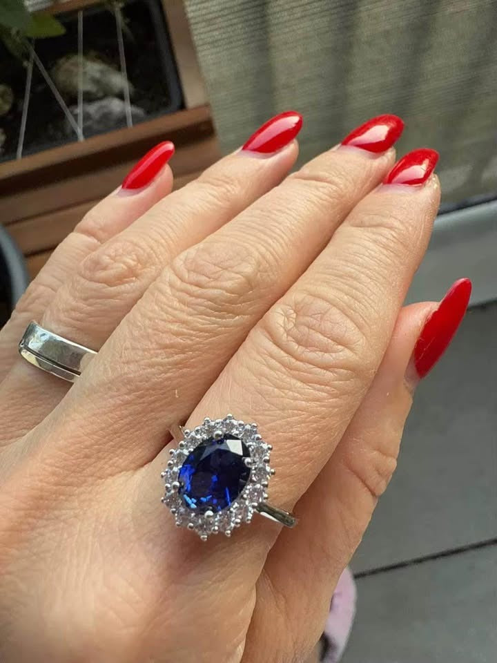 A beautiful sapphire Diana ring worn on a hand with vibrant red fingernails, highlighting its design.