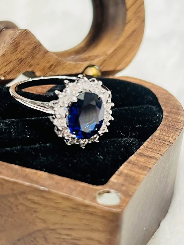 Side view of a stunning sapphire Diana ring with a diamond-like halo, displayed in a wooden heart box.