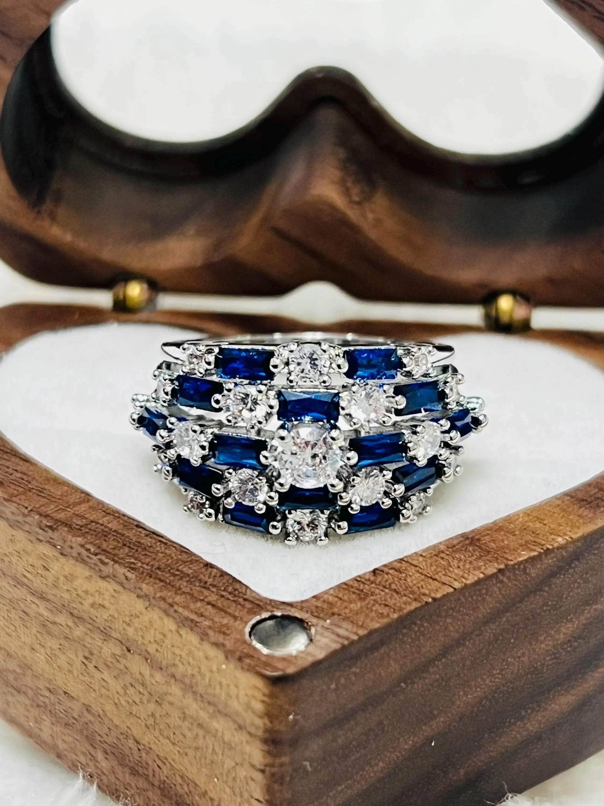 Close-up of a sapphire and diamond statement ring, nestled in a charming heart-shaped wooden jewelry box.