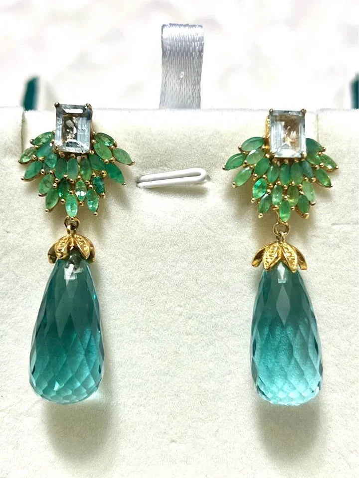 A pair of showstopper dangle earrings. The design highlights faceted aquamarine drops and emerald cluster accents.