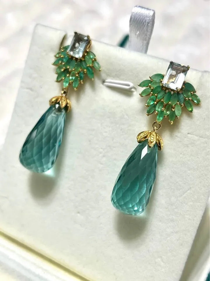  Close-up side view of a pair of dangle earrings. Showcases the natural emerald, topaz, and aquamarine gemstones.