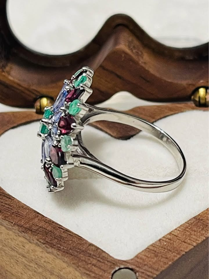 Side profile of a sterling silver ring. Features a floral cluster design with tanzanite, emerald, and rhodolite garnet