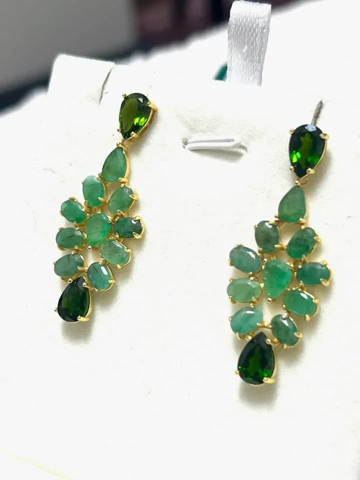 Angled view of elegant sterling silver earrings, featuring a cluster of natural emeralds and striking green dropside gems.