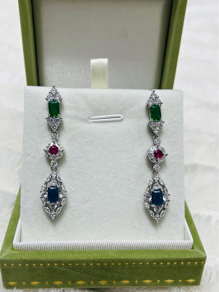 Sterling silver drop earrings with emerald, ruby, and sapphire stones, displayed in an open green jewelry box.