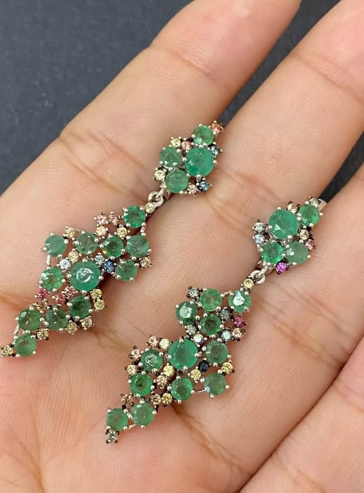 A pair of elegant sterling silver earrings with natural emeralds and sapphires in a decorative black gift box.