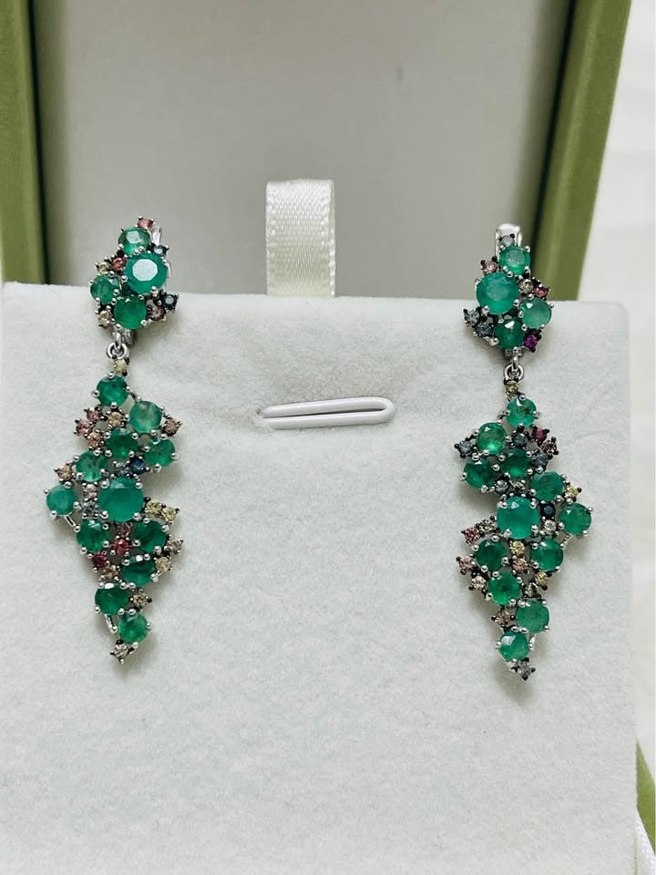 Sterling silver drop earrings featuring natural emerald and sapphire gems, beautifully displayed on a white stand.