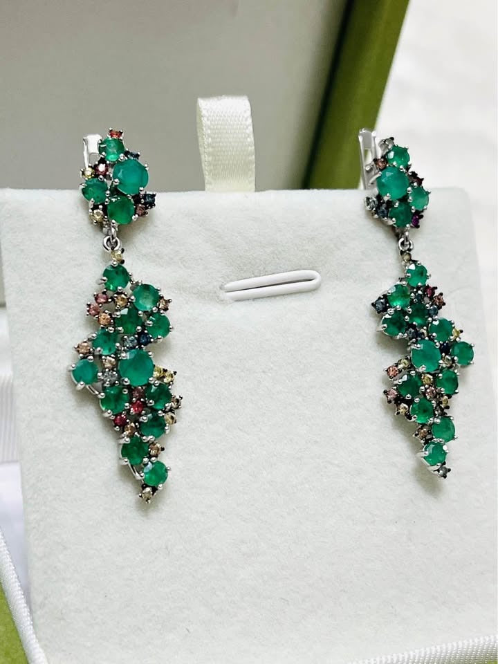 Top-down view of a pair of sterling silver earrings, highlighting the circular arrangement of emerald and sapphire stones.