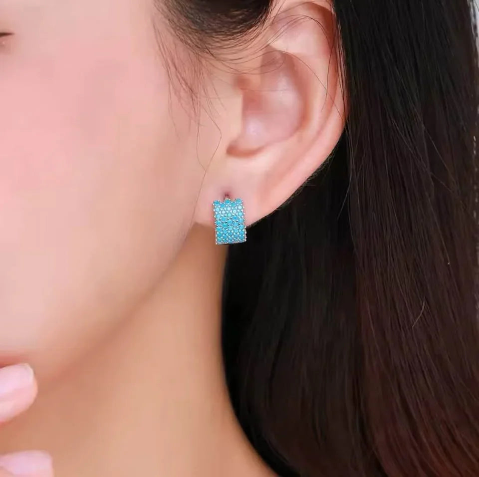 A woman modeling wide sterling silver hoop earrings with a beautiful pave setting of real turquoise stones.