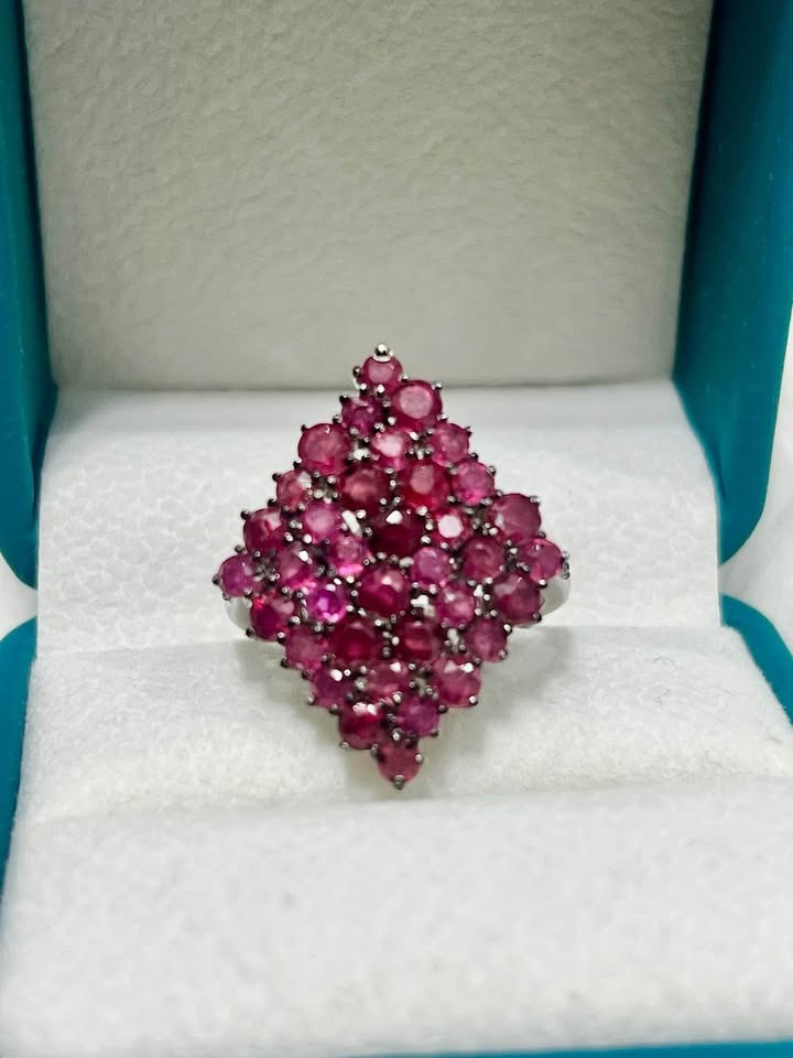 Close-up of a sterling silver ring with a dazzling cluster of natural rubies and diamonds, shown in a gift box.
