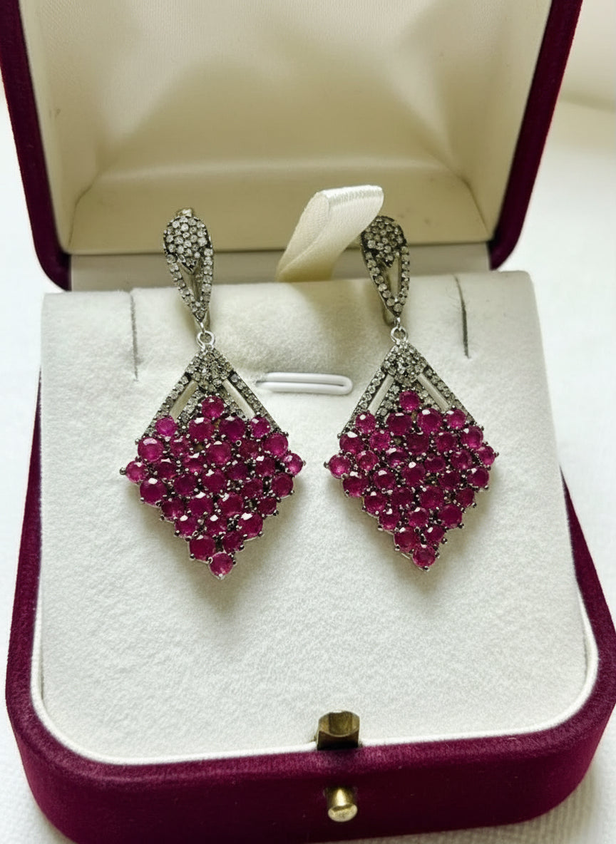 Angled view of sterling silver dangle earrings, showcasing the clustered natural rubies and diamond-studded top.