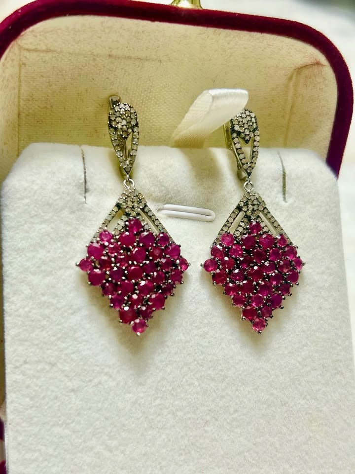 Frontal view of a pair of sterling silver earrings, featuring a striking diamond shape filled with rubies.
