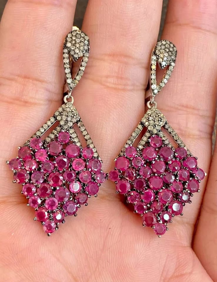 A pair of genuine sterling silver earrings with a cluster of natural rubies and diamond accents held in a hand.