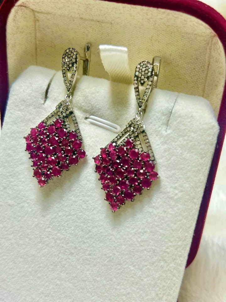 A pair of genuine sterling silver earrings with natural rubies and brilliant diamond accents, displayed in a box.
