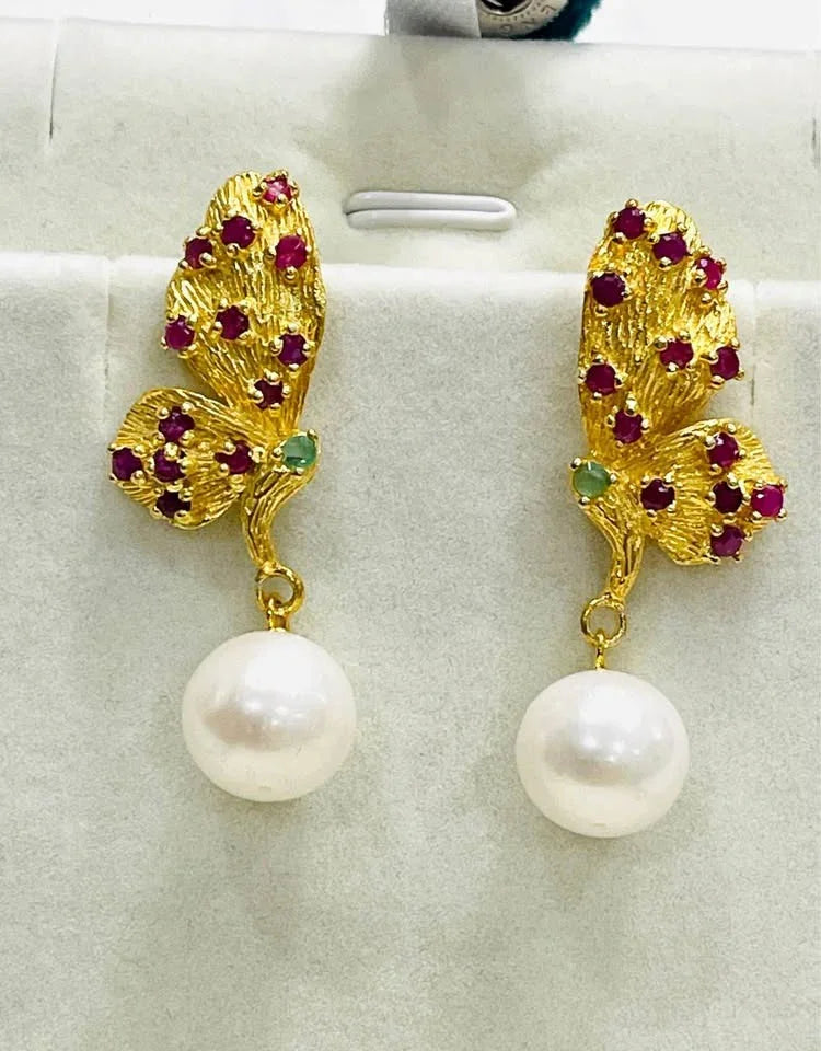 Close-up of artisan butterfly earrings with natural rubies, emeralds, and lustrous pearls on a white display.
