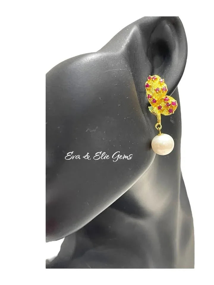 Handamde ruby, emerald, and pearl butterfly earrings modeled on a mannequin to show size and style.