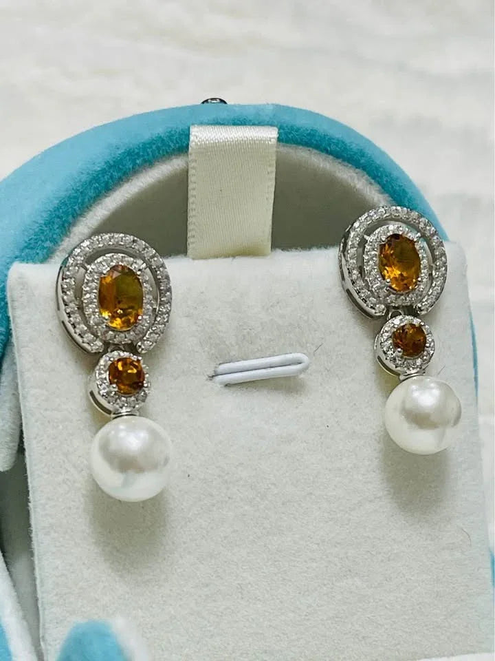 Elegant natural sterling silver earrings with vibrant citrine stones and cultured pearls on a soft blue display.