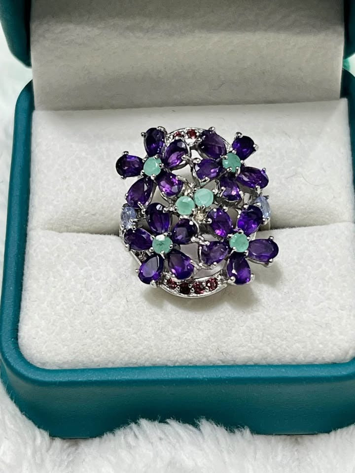 Intricate floral ring in sterling silver, showcasing natural amethyst petals and emerald centers.