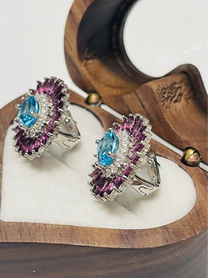 Angled view of Swiss blue topaz and rhodolite garnet earrings in silver, showing earring backs.