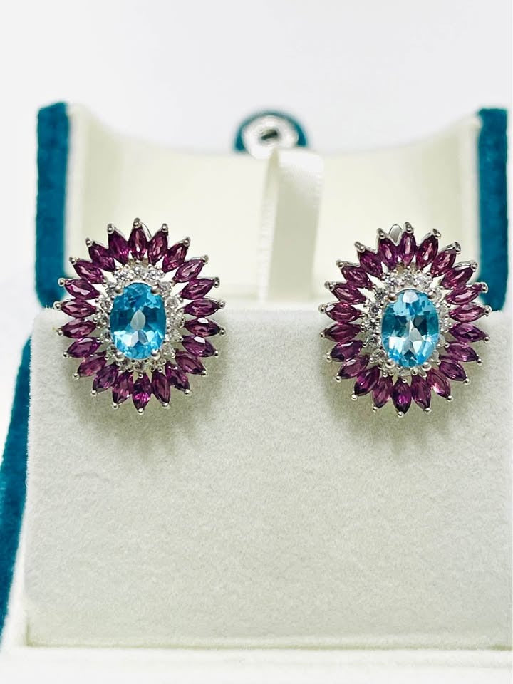Front view of sterling silver earrings with vibrant Swiss blue topaz and rhodolite garnet halo.
