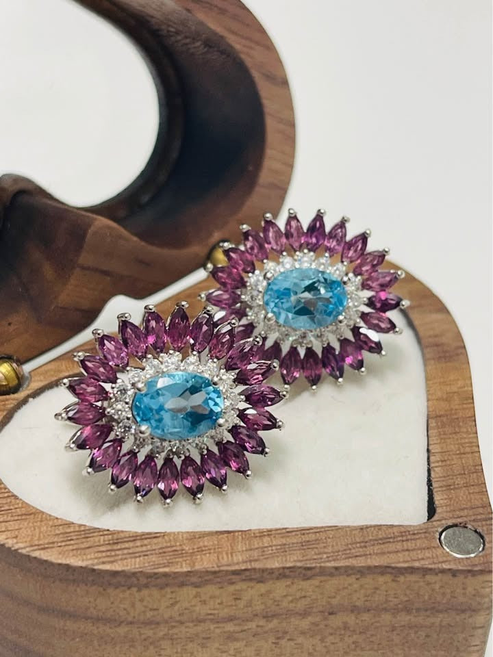 Pair of exquisite Swiss blue topaz and rhodolite garnet earrings in an open heart-shaped box.