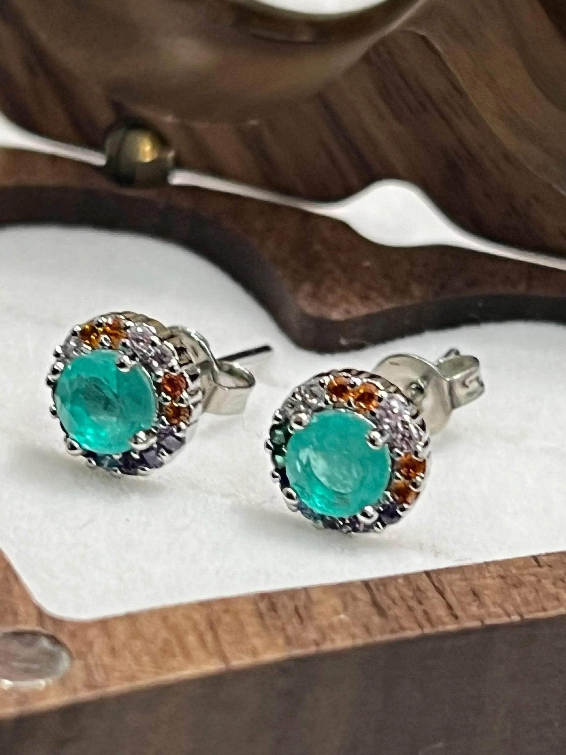Close-up of vibrant teal Paraiba Tourmaline stud earrings with multi-gemstone accents, sterling silver.