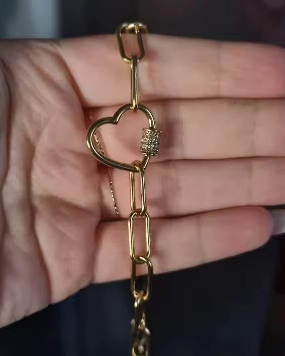 Close-up of a vermeil paperclip chain necklace featuring a detailed pave heart clasp held in hand.