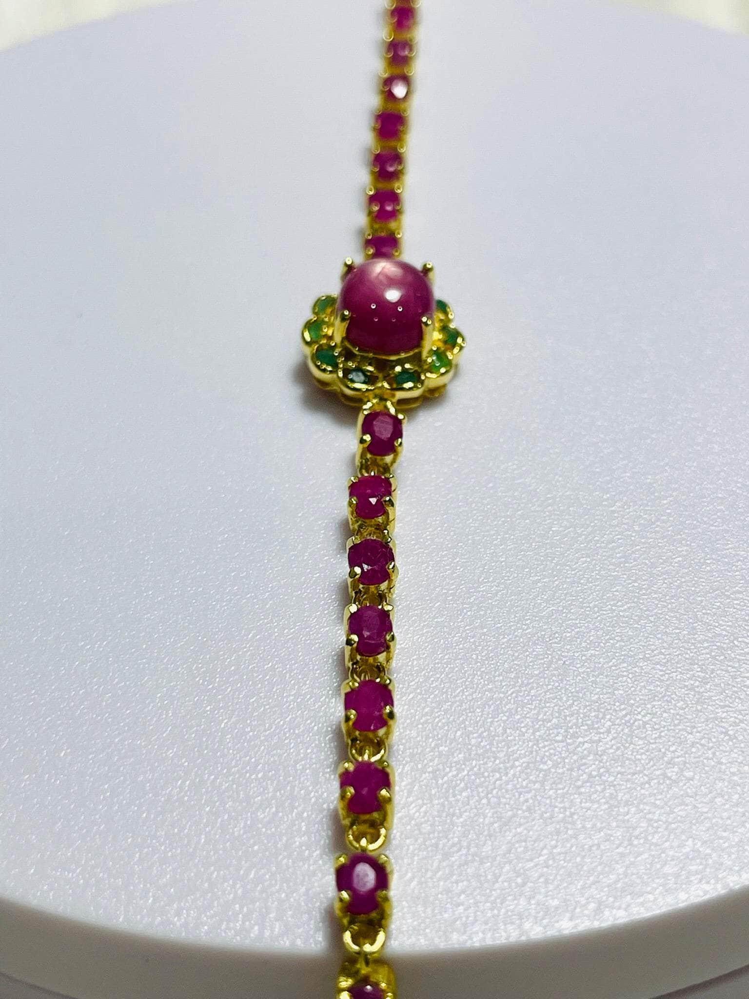 Vertical close-up of Gold bracelet with radiant ruby cabochon, surrounded by green emeralds and ruby links.
