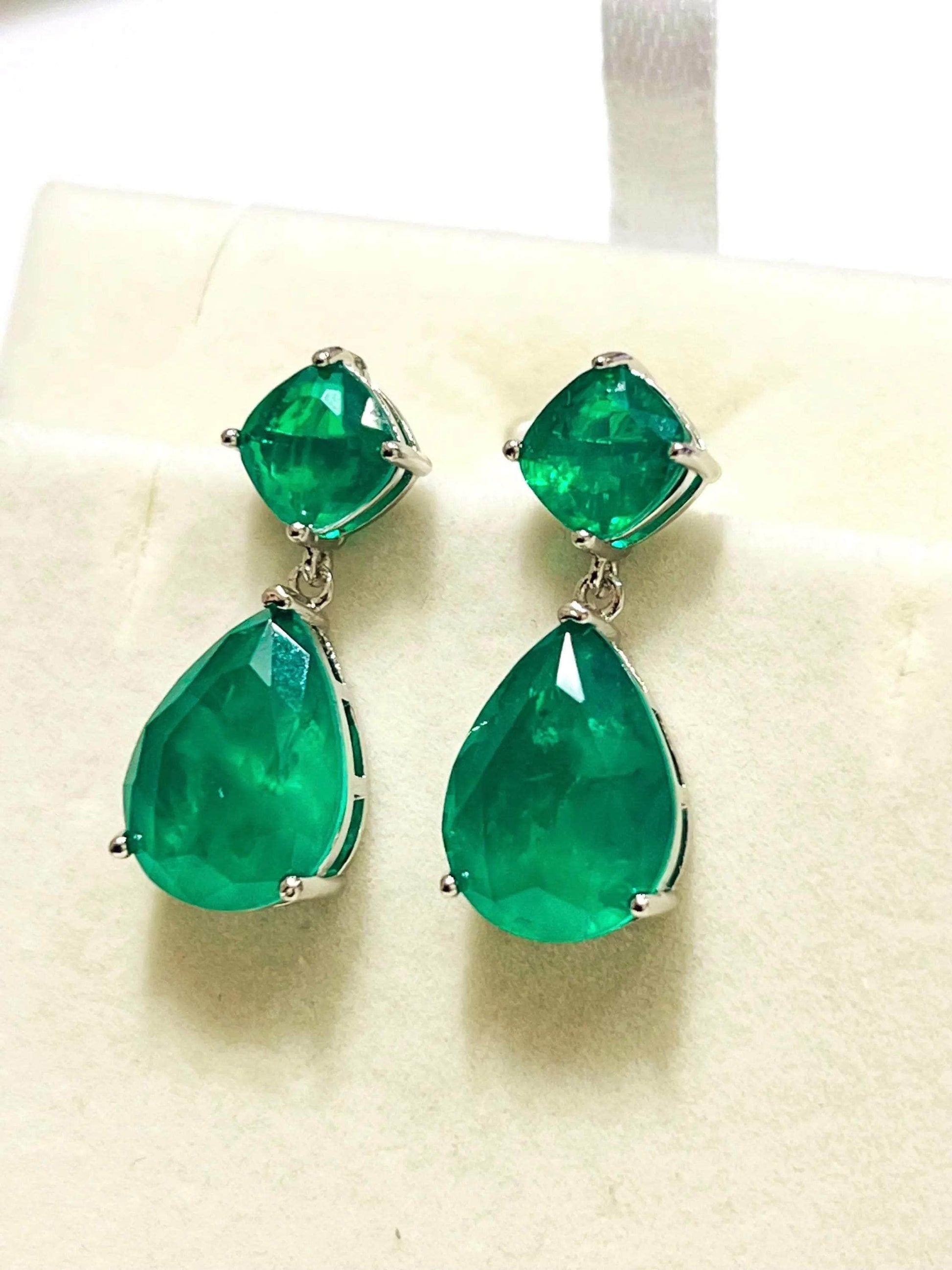 Top-down perspective of Zambian emerald doublet earrings in gold and rhodium, highlighting their pear and cushion cuts.
