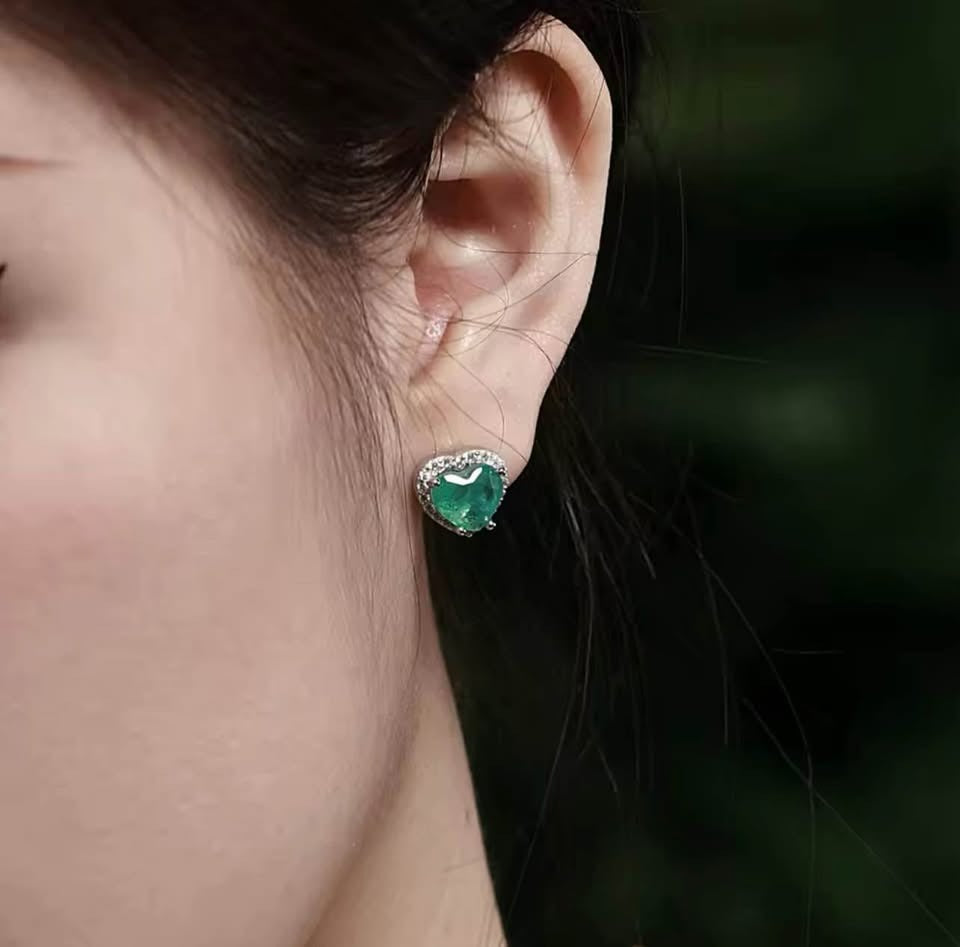 Natural Zambian emerald heart-shaped earring with diamond halo on a woman's left ear, close up.