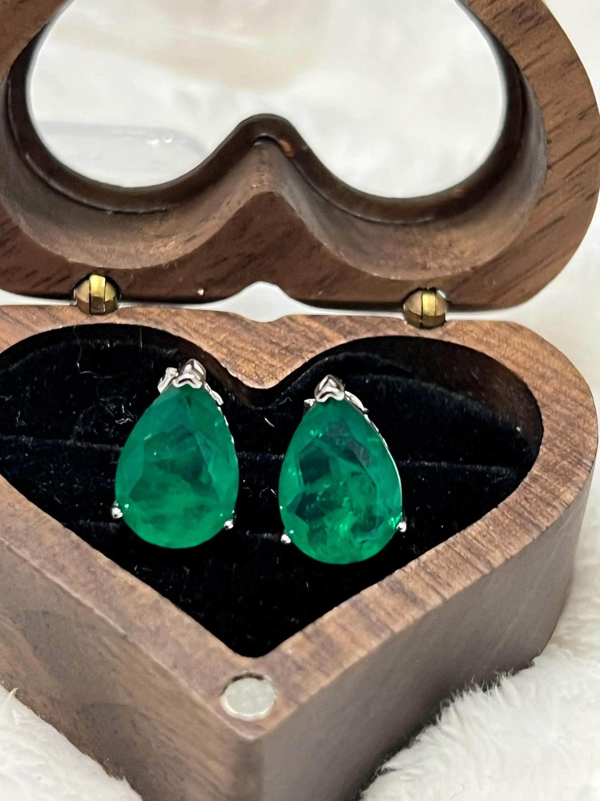 Angled view of vibrant Zambian emerald stud earrings, showcased in a charming wooden heart-shaped box.