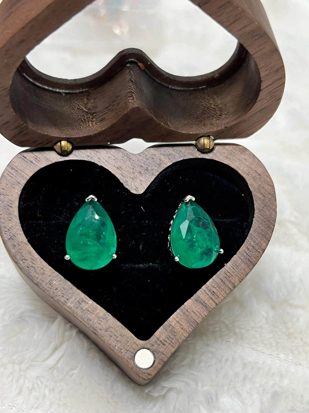 Pear-shaped Zambian emerald stud earrings displayed beautifully in an open heart-shaped wooden box.
