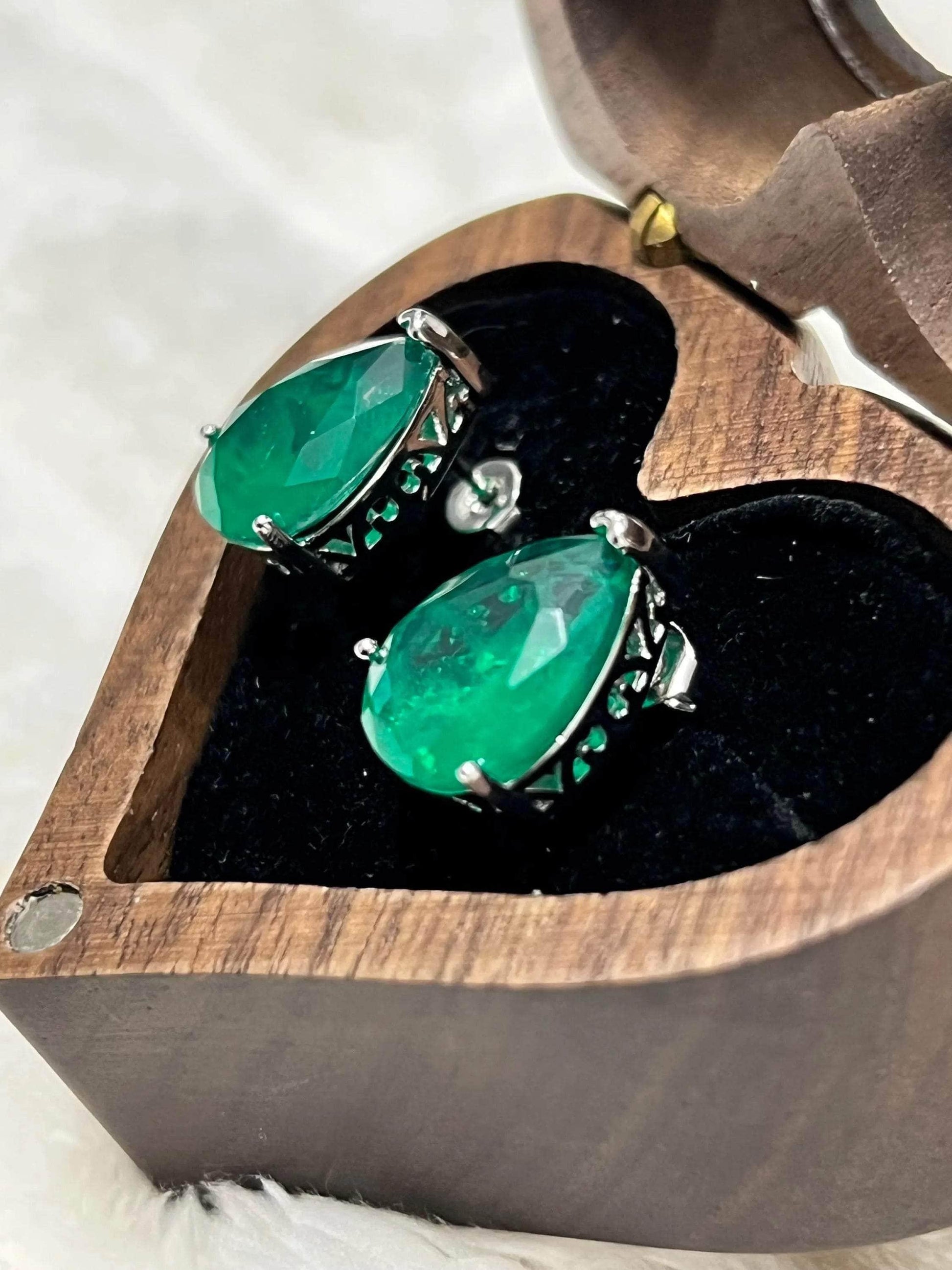 Top-down angle of stunning Zambian emerald stud earrings in a wooden heart-shaped presentation box.